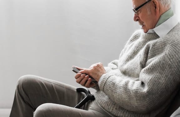 Older mal sitting on couch looking down at his phone