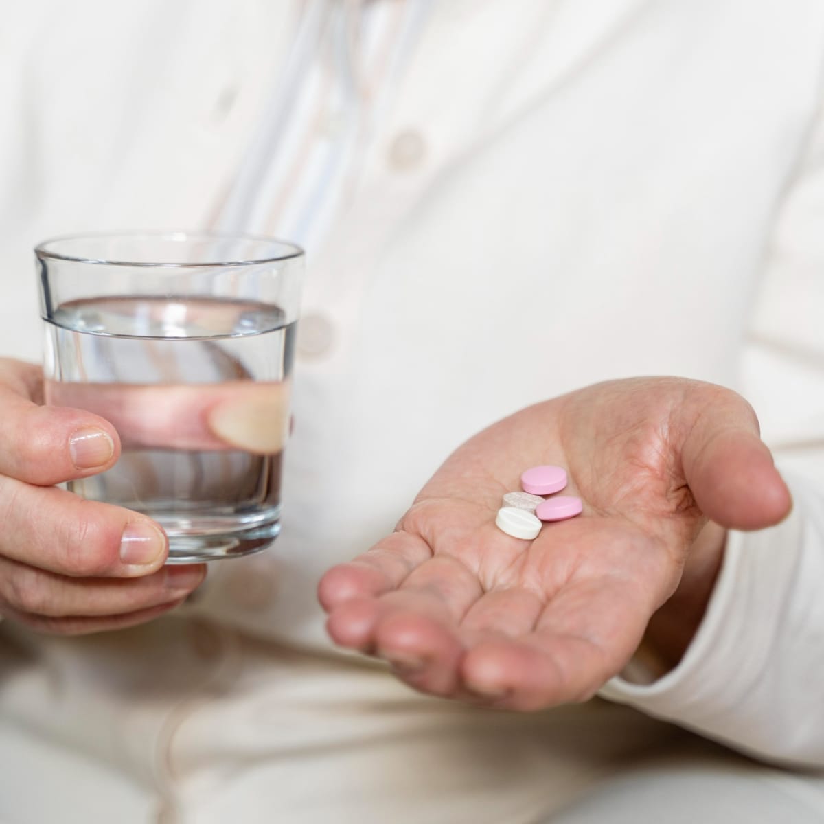 Close up of hands holding a glass of water and some pills
